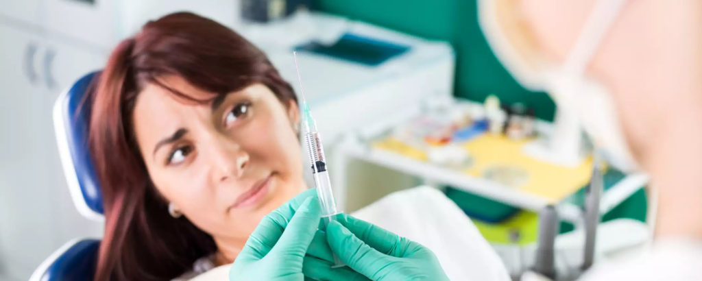 Девушка сидит в кресле у стоматолога, врач держит в руках шприц с лекарством